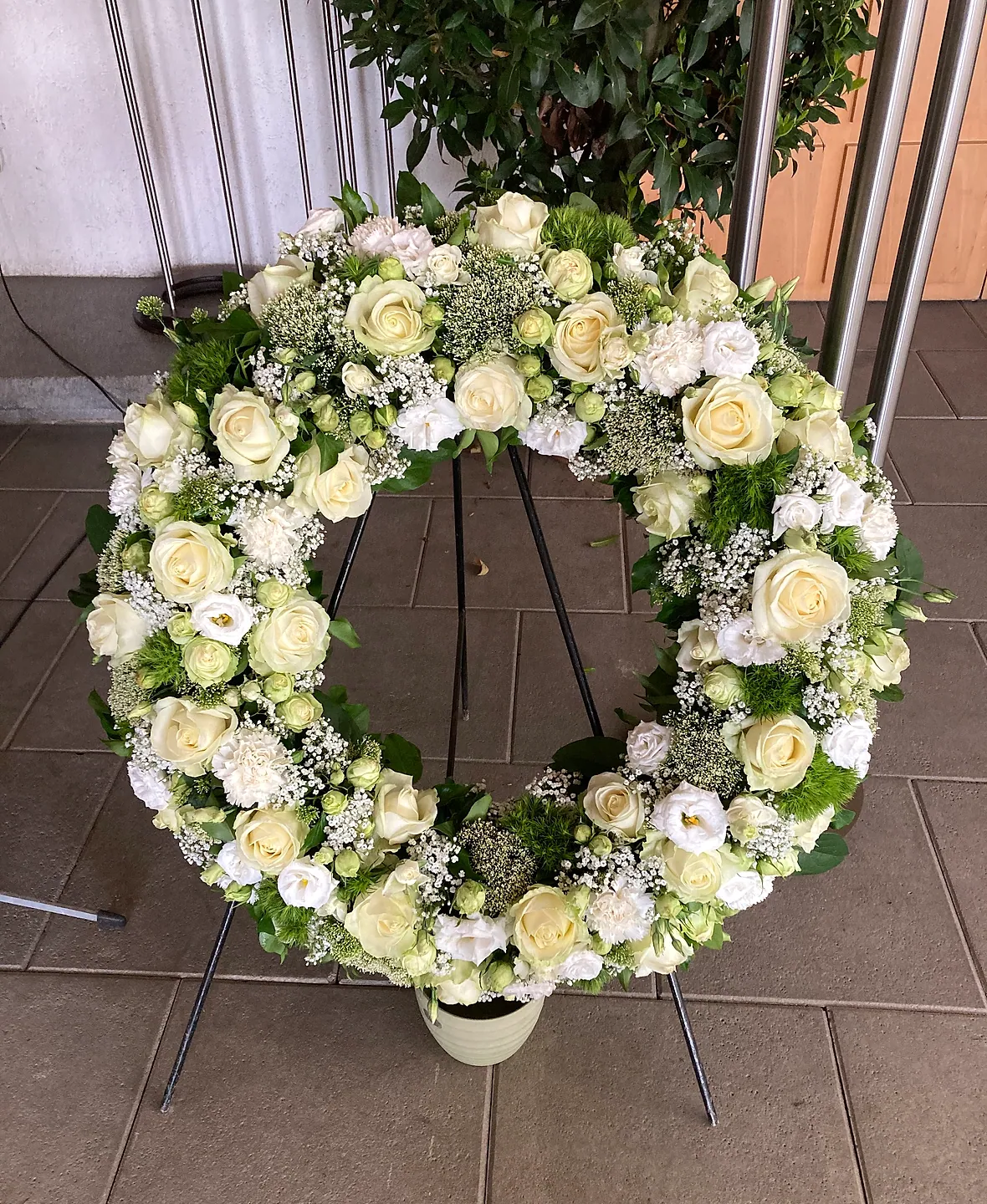 Trauerkranz aus weißen und grünen Blüten auf einem Ständer
